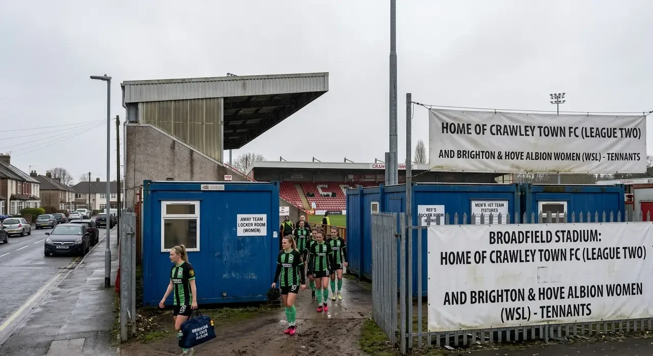 An Arsenal player taking a shot in front of empty seats at a shared WSL stadium.
